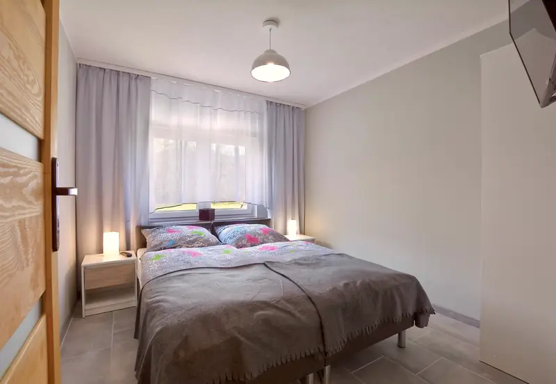 Apartament 1 – sypialnia z podwójnym łóżkiem, szarą narzutą i kolorowymi poduszkami